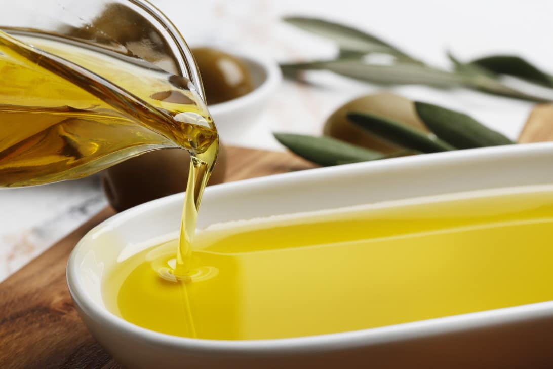 Composition of green olives in oil, olive branch, gravy boat on a marble background. Space for text.